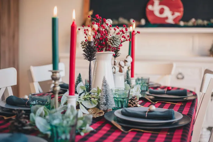 A Christmas table on a red buffalo-check cloth with green and red taper candles and a jug of red berries