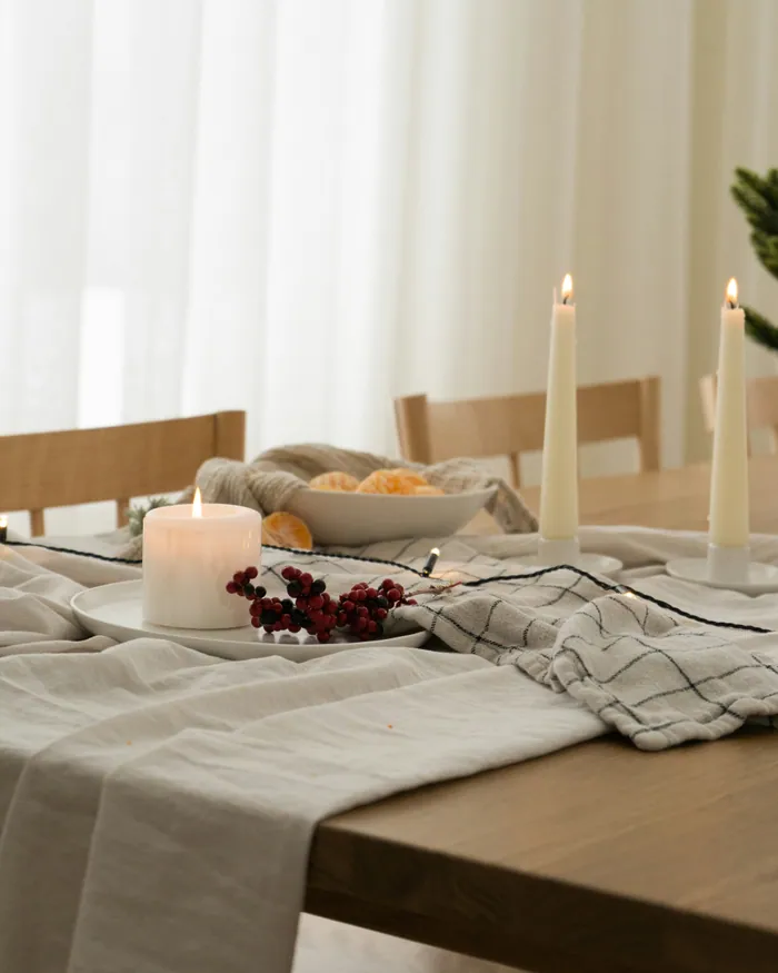 A pared-back table with a crumpled linen runner, a bowl of clementines and slim white candles