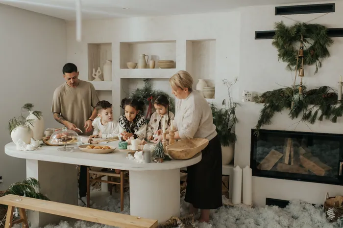 A grandmother, a father and three children making biscuits together around a white oval table, a wreath on the wall behind