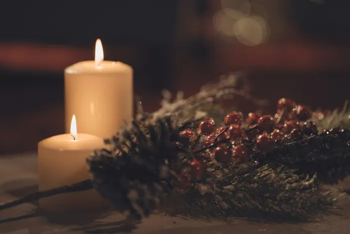A single white pillar candle lit beside a garland of pine and red berries