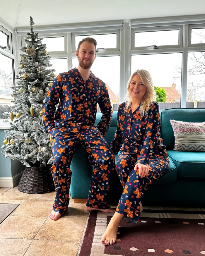 A couple in matching navy floral pyjamas sitting on a sofa beside a frosted tree
