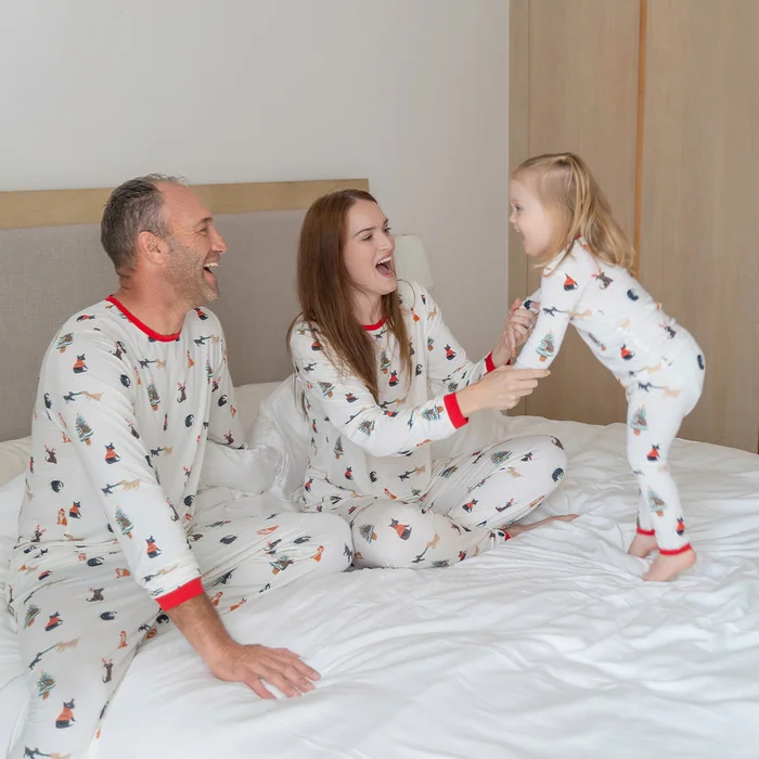 Two parents and a little girl in matching white Christmas print pyjamas playing on a bed