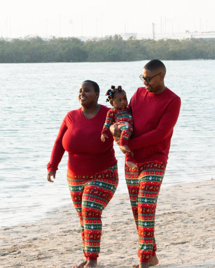 A family in red tops and matching Christmas print pyjama trousers walking along a beach