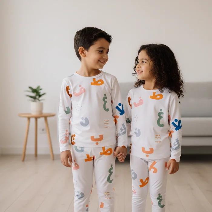 Two children in white pyjamas printed with colourful Arabic letters