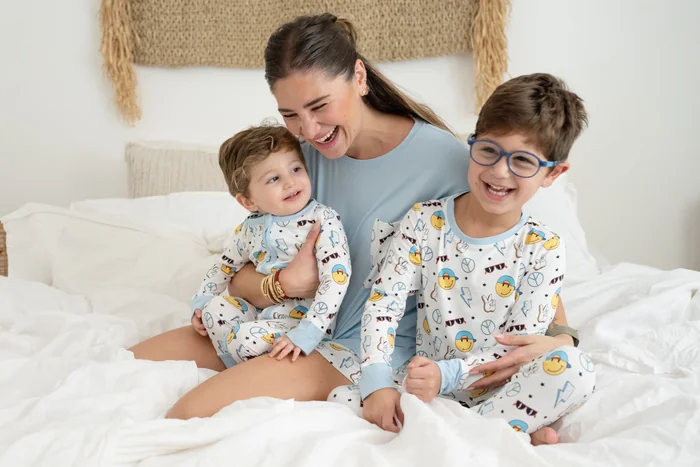 A mother and two boys in matching printed pyjamas on a white bed