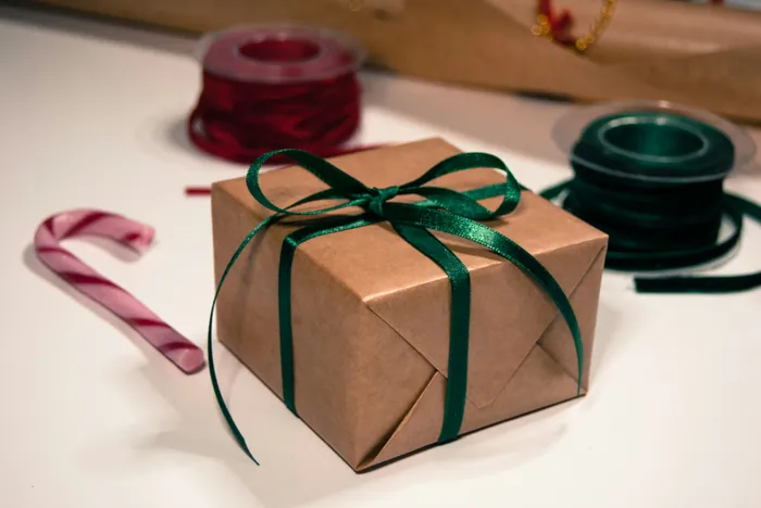 A box wrapped in brown paper and tied with a green ribbon beside a spool of red ribbon