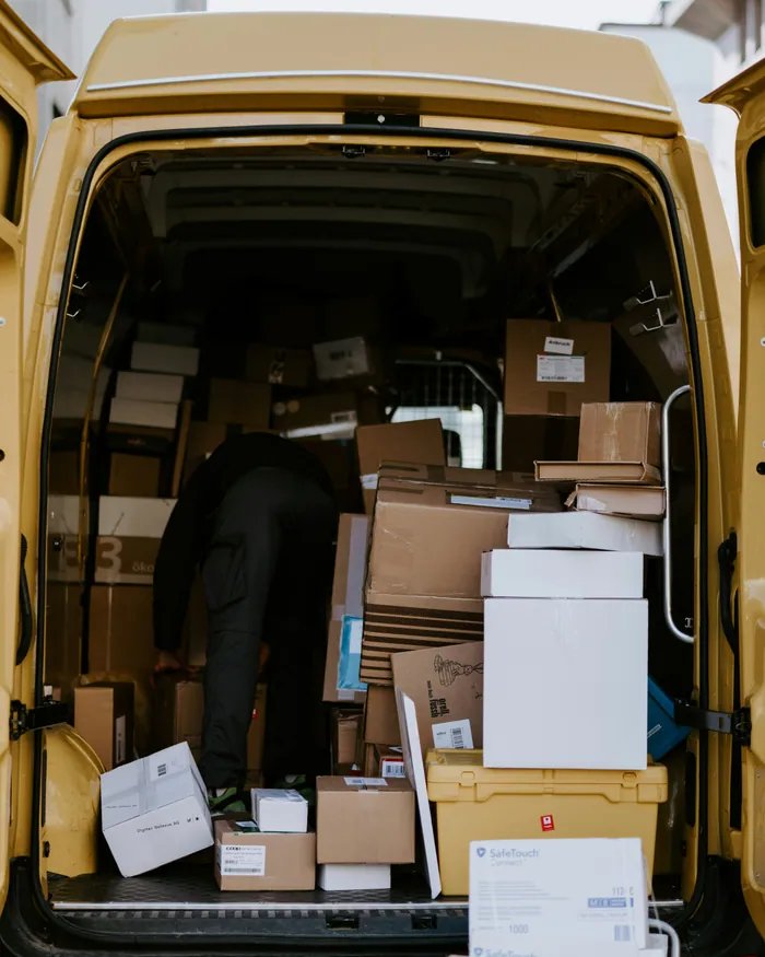 A courier loading cardboard boxes into the back of a yellow delivery van