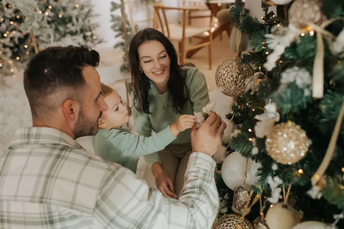 A family decorating a flocked Christmas tree together, the little boy reaching up to hang a bauble