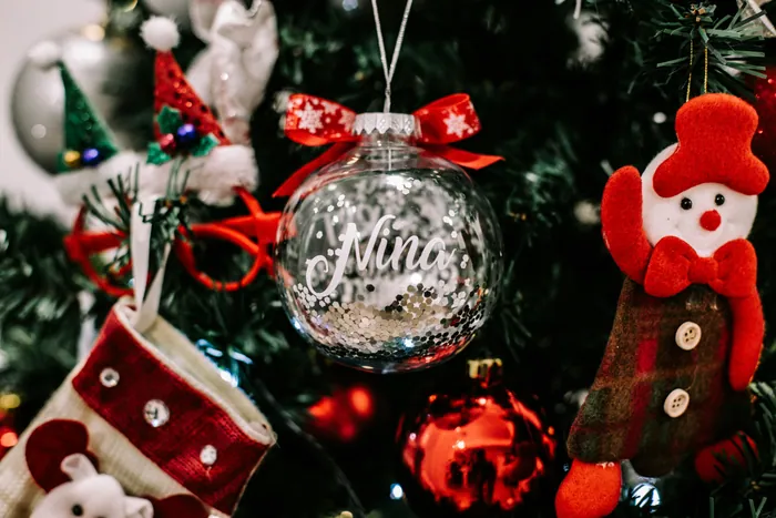A clear glass bauble painted with the name Nina in white, tied with a red bow