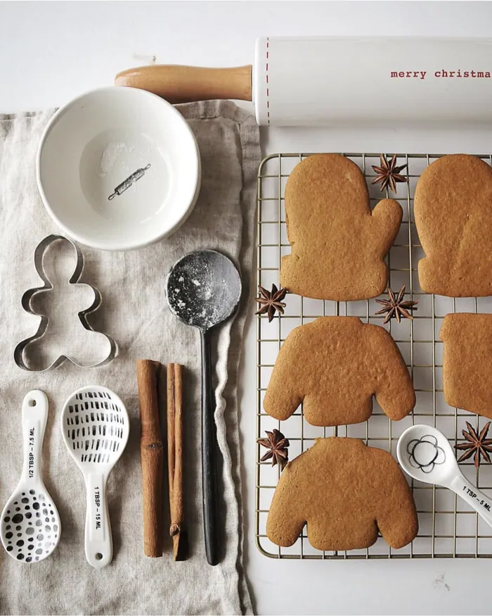 Gingerbread biscuits shaped like mittens and jumpers cooling on a wire rack beside cutters and spoons