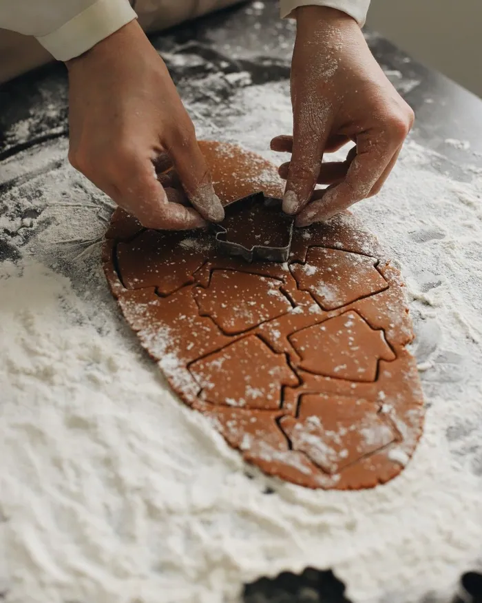 Floury hands cutting Christmas tree shapes from rolled gingerbread dough