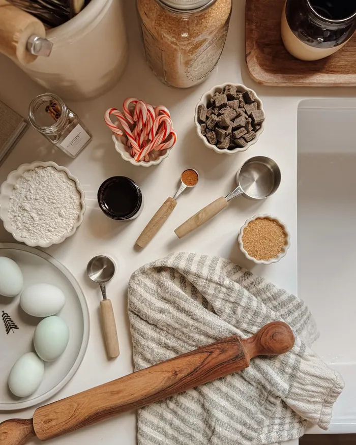 Bowls of chocolate, candy canes, sugar and eggs laid out with a rolling pin on a white counter