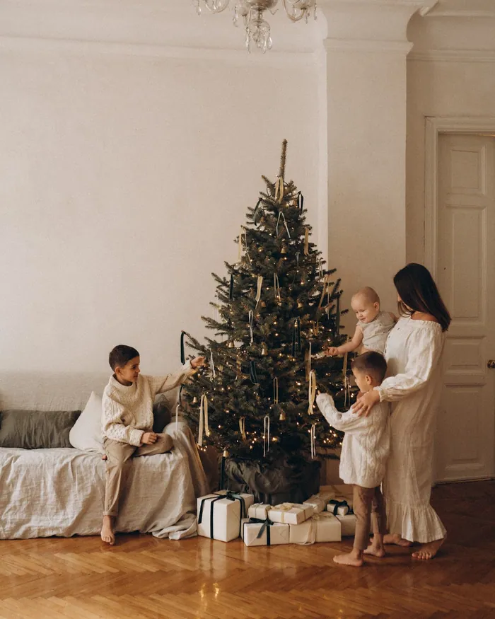 Children decorating a Christmas tree with their parents in a pale room with a chandelier