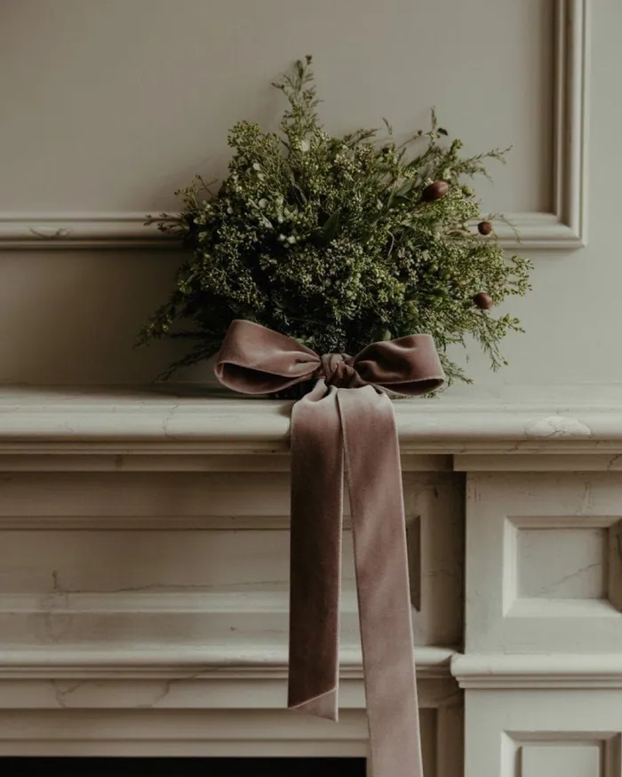 A bunch of fresh fir branches tied with a brown velvet ribbon, hanging on a pale panelled wall