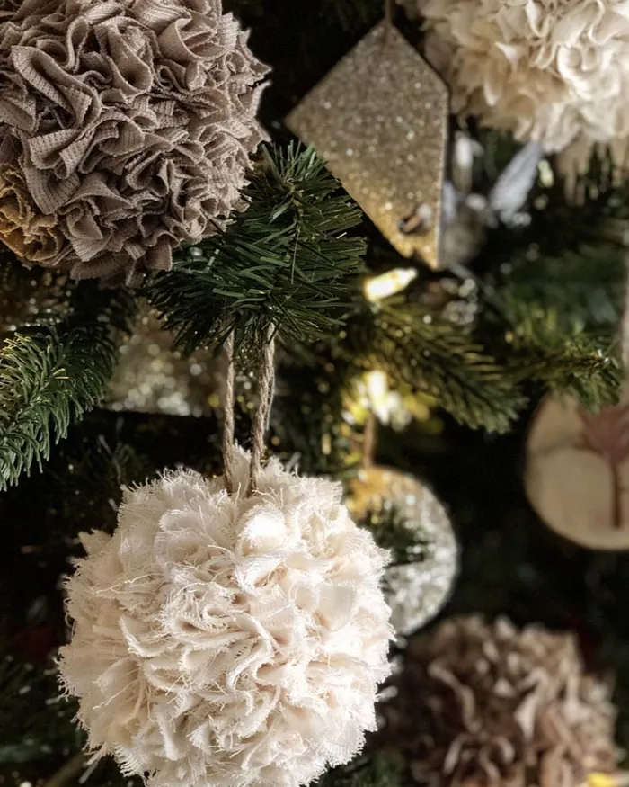 Close-up of a Christmas tree hung with a fluffy cream ball ornament and soft fabric decorations