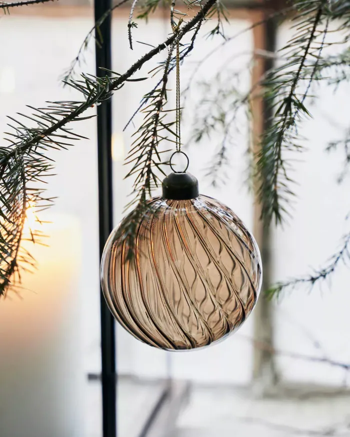 A smoky glass bauble hanging from a bare pine branch beside a lit candle
