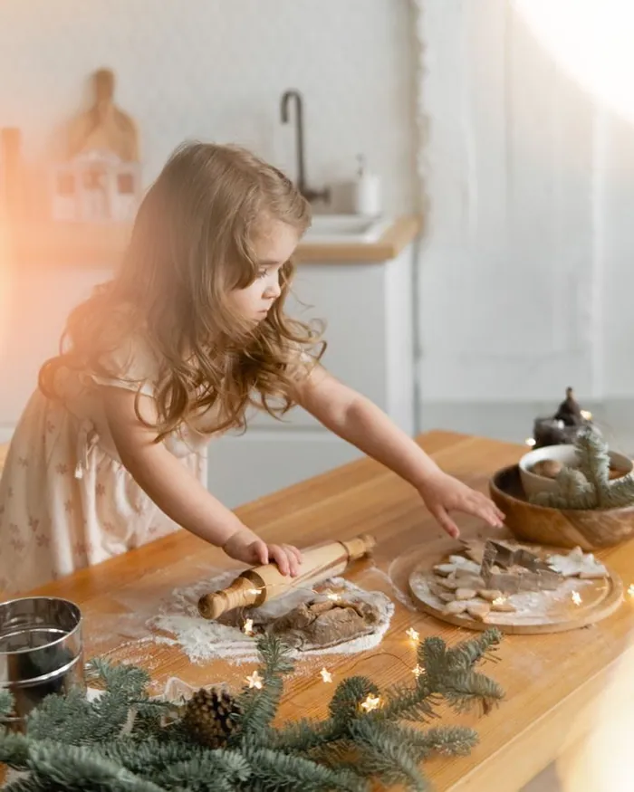 A little girl in a pink dress pressing shapes into dough at a wooden kitchen table