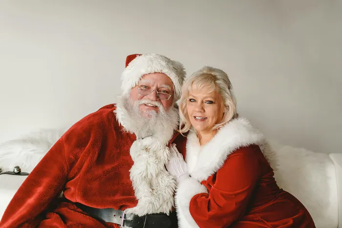 A smiling Santa Claus with a real white beard and gold-rimmed glasses, Mrs Claus beside him