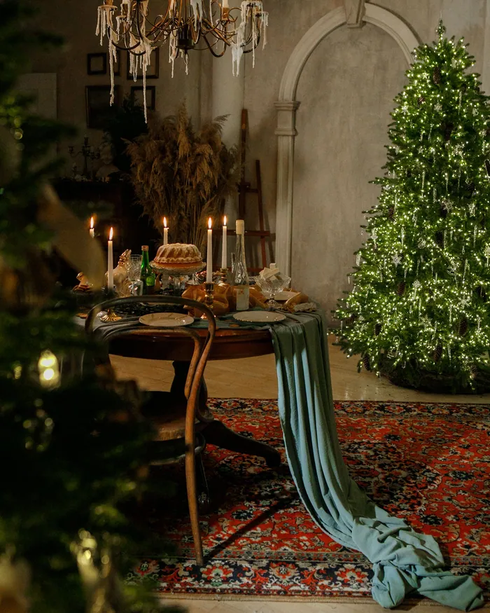 A candlelit room laid for a party, with a long table, chandeliers and a tall Christmas tree