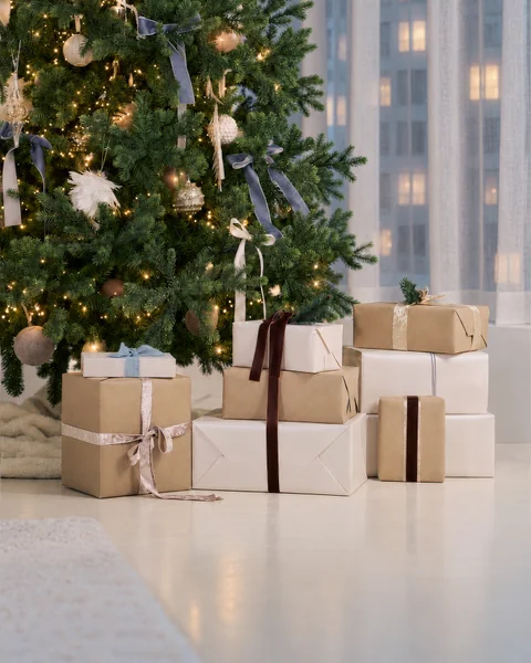 Presents in kraft and white paper tied with ribbon beneath a decorated Christmas tree