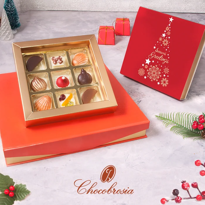 An open gold box of chocolates on a red Christmas gift box