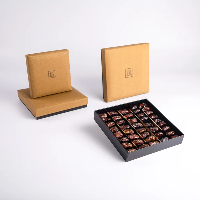 An open box of chocolate-dipped dates in front of two closed gold gift boxes