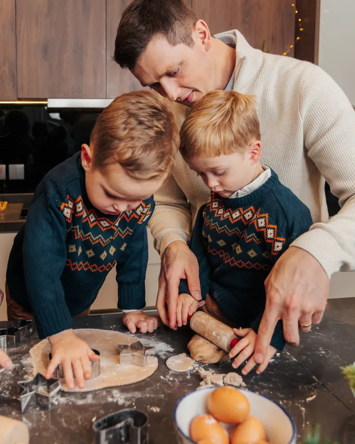 A father in a cream jumper and two boys in fair isle cutting gingerbread shapes