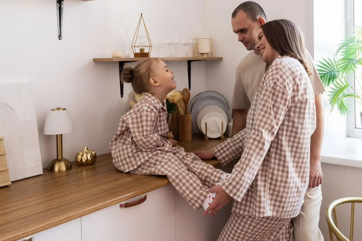 A mother and daughter in matching brown gingham pyjamas at the kitchen counter, the father beside them