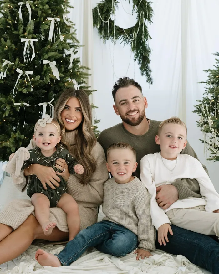 A family in oatmeal, olive and cream knits and denim sitting together in front of the tree