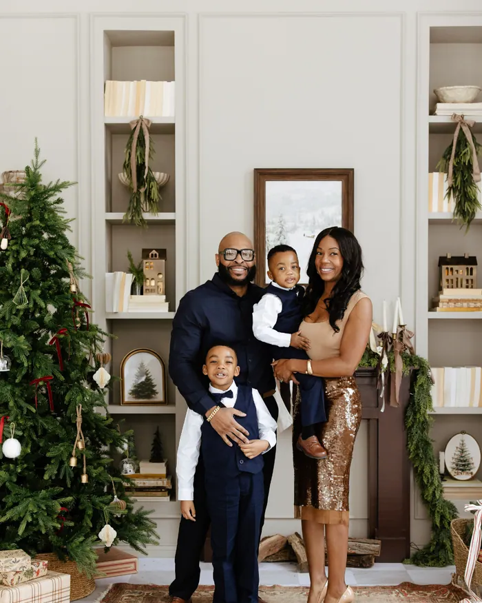 A family in navy and gold standing on a rug beside the tree, the boys in waistcoats and bow ties