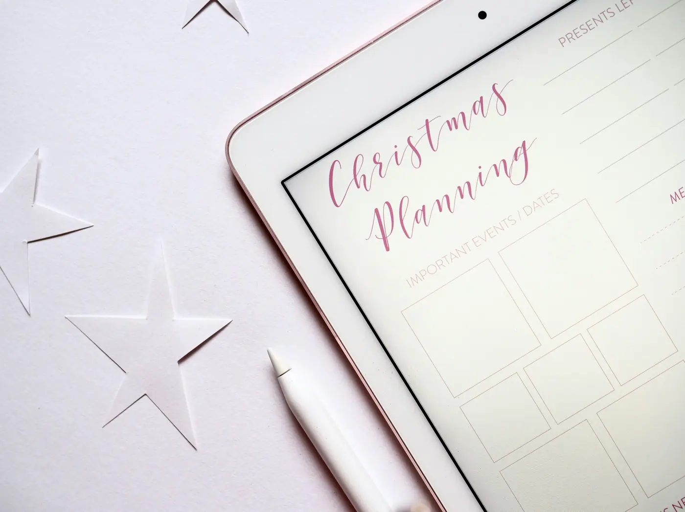 A tablet showing a Christmas planning page beside a stylus and paper stars