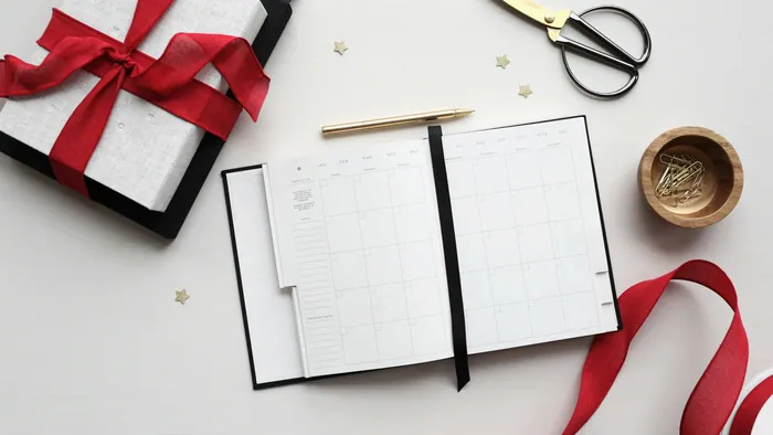 An open planner with a monthly grid and a gold pen on a white desk
