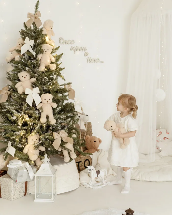 A small girl in white looking up at a Christmas tree decorated with teddy bears and bows