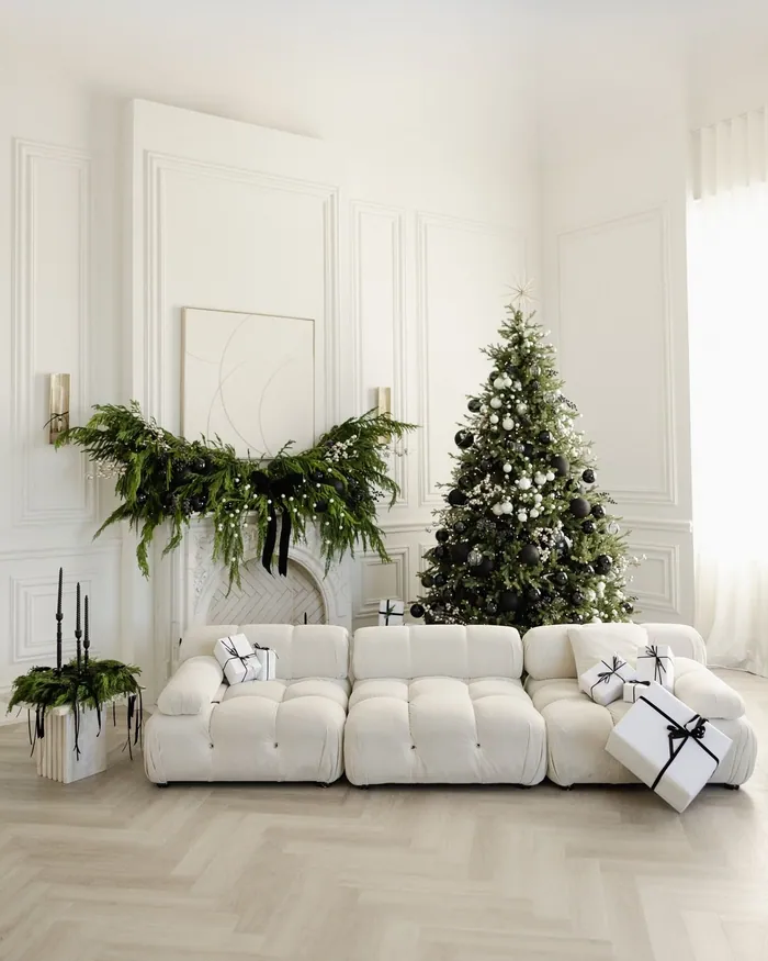 A fir garland hung across a white wall above a cream sofa, a decorated tree beside it