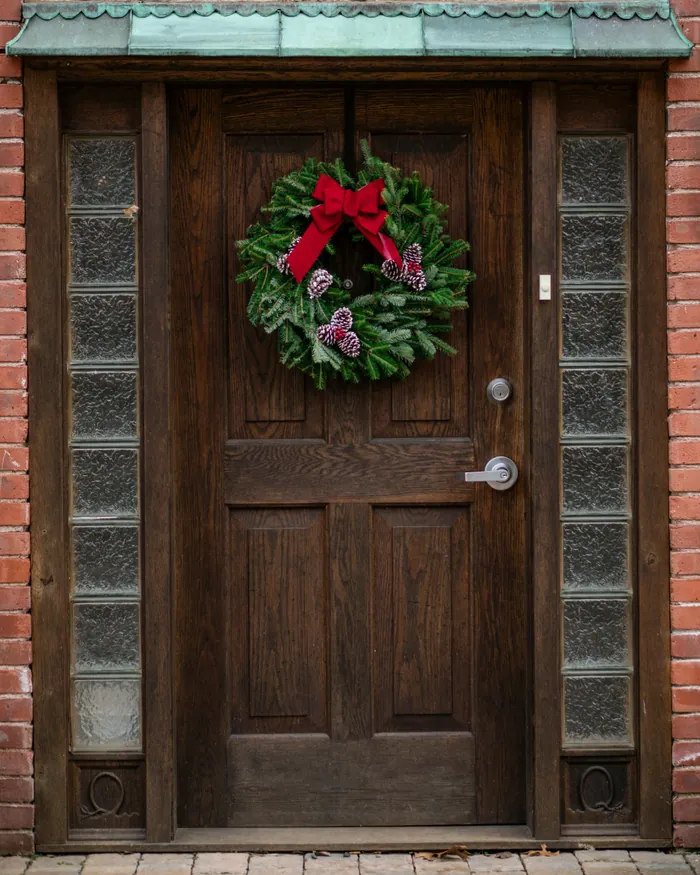 A fir wreath with a red bow hanging on a dark wooden door
