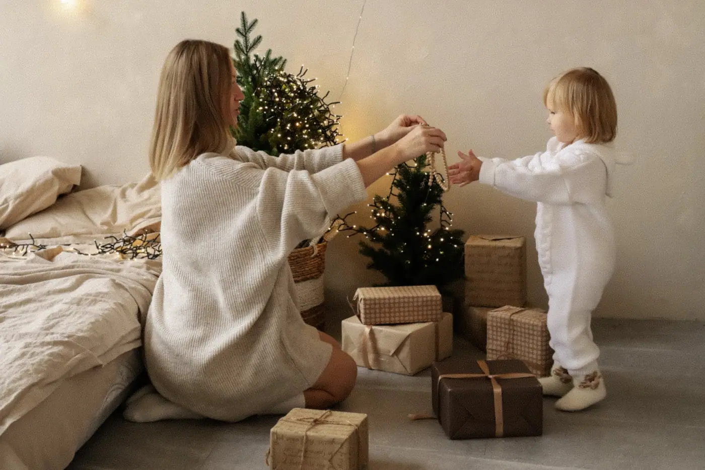 A mother and her small daughter arranging parcels beneath a little tree, two fir wreaths hung on the wall behind them