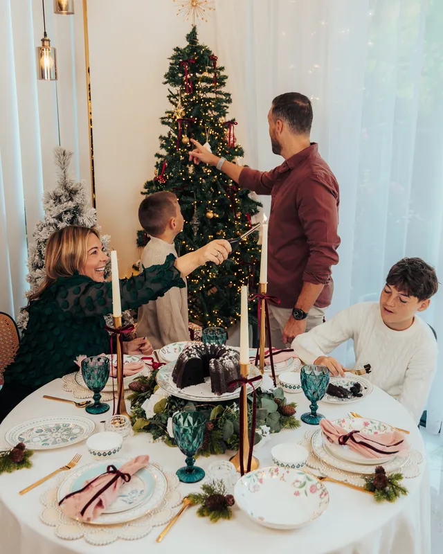 A family decorating the tree behind a laid table with lit candles