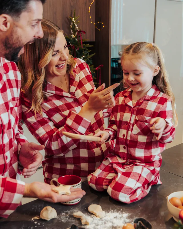 A mother and daughter in red gingham pyjamas laughing over the baking counter, flour everywhere