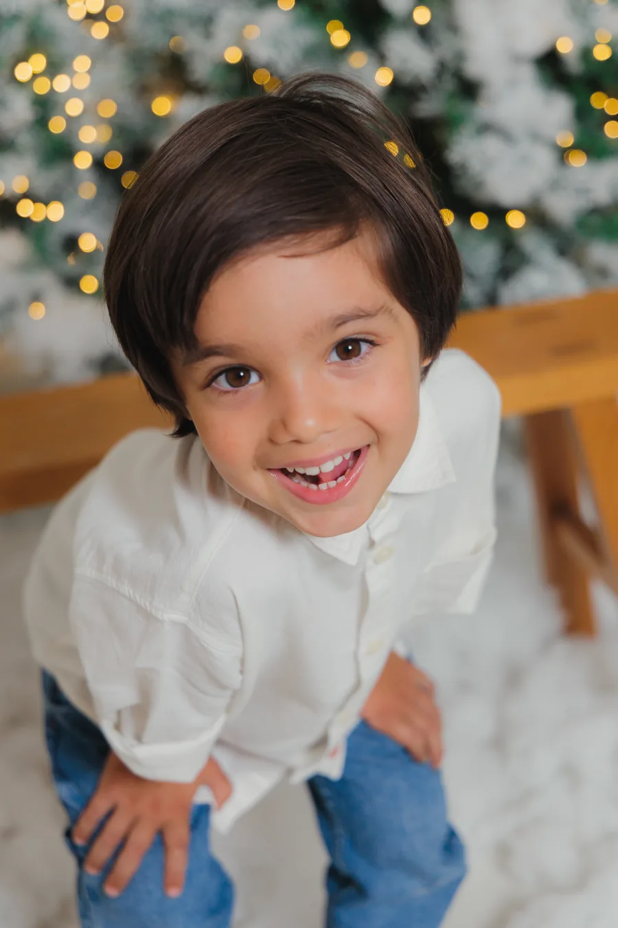 A boy in a white shirt grinning up at the camera in front of the flocked trees