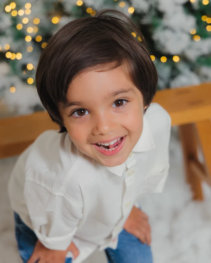 A boy in a white shirt grinning up at the camera in front of the flocked trees