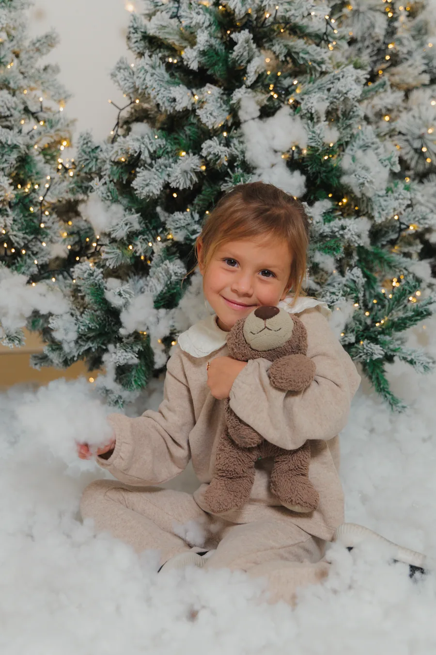 A small girl in cream hugging a teddy bear in deep snow