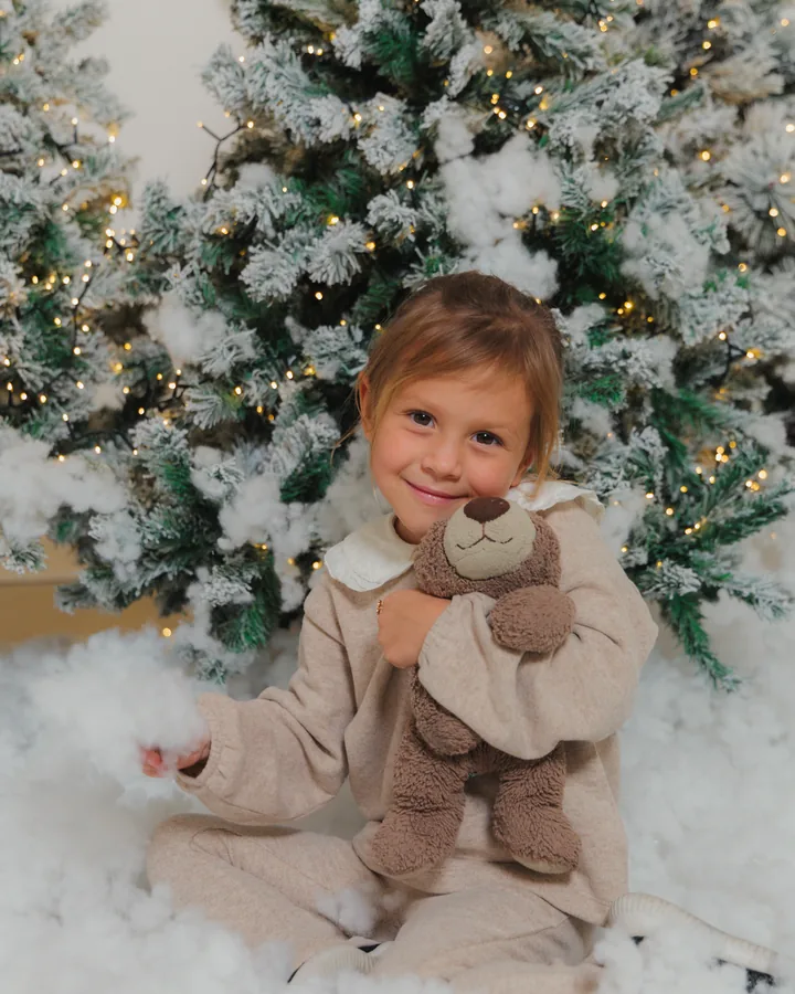 A small girl in cream hugging a teddy bear in deep snow