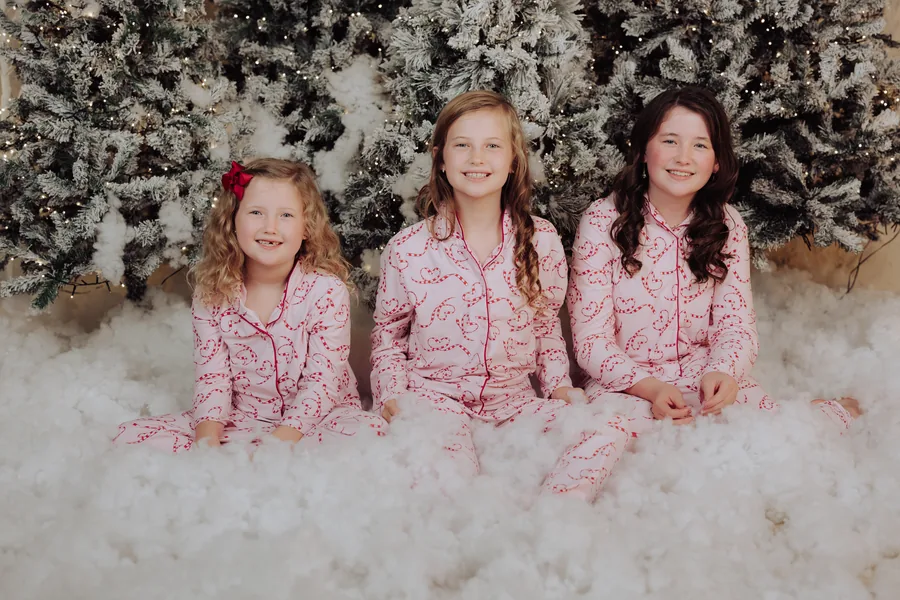 Three sisters in pink pyjamas sitting together in the snow