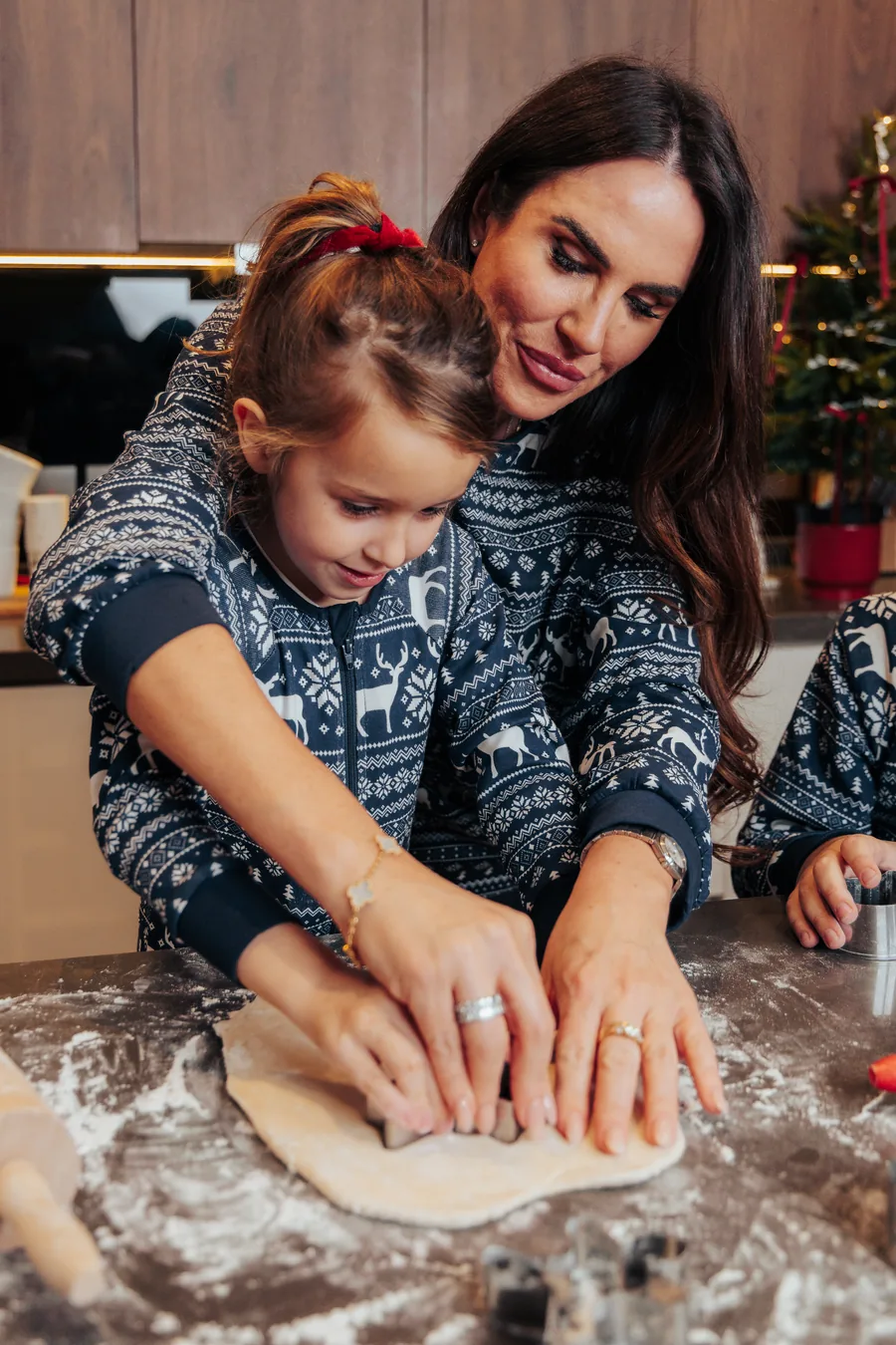 A mother and daughter in matching navy jumpers pressing dough on a floured counter