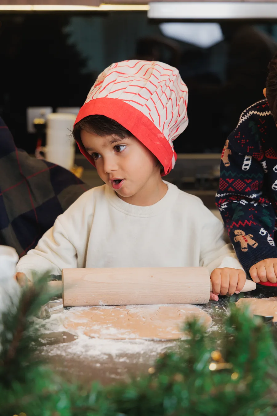 A boy in a red knitted hat with a rolling pin, flour everywhere