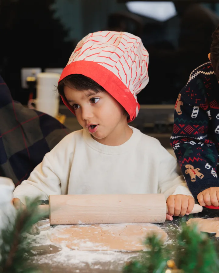 A boy in a red knitted hat with a rolling pin, flour everywhere