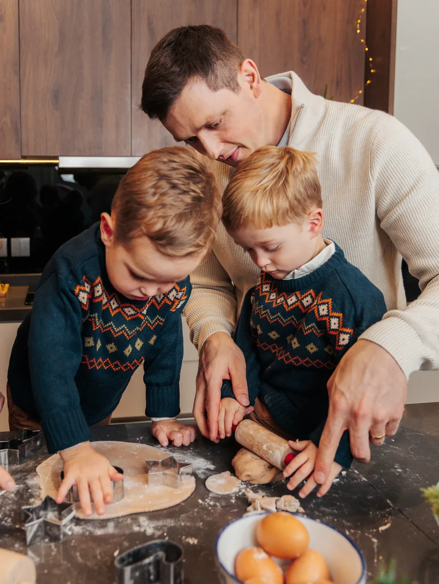 A father and two boys in fair isle jumpers cutting gingerbread shapes