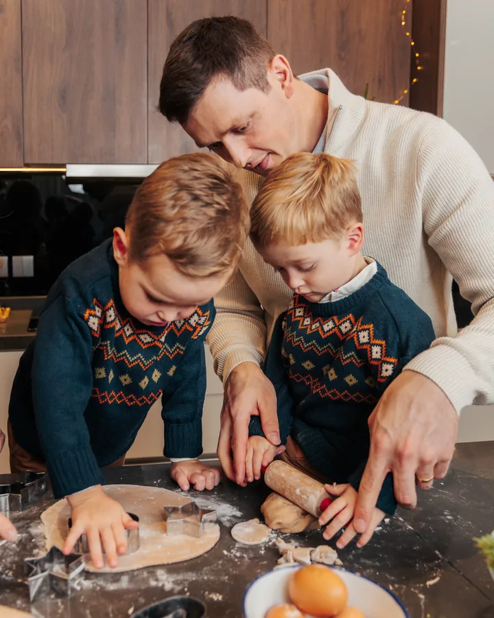 A father and two boys in fair isle jumpers cutting gingerbread shapes