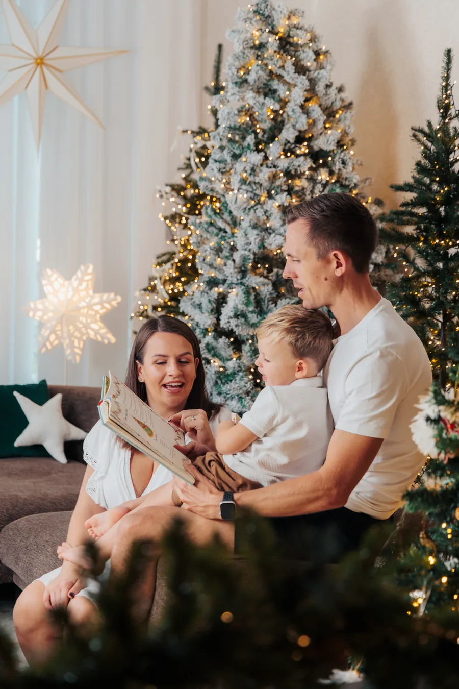 A mother and father on a sofa with their small son between them, a lit tree and a paper star behind