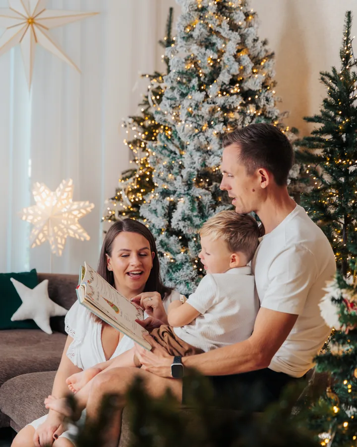 A mother and father on a sofa with their small son between them, a lit tree and a paper star behind